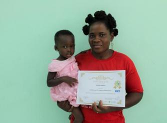 Susana Amble, shows off her ICT certificate while holding her youngest child, 3-year-old Precious Aidoo
